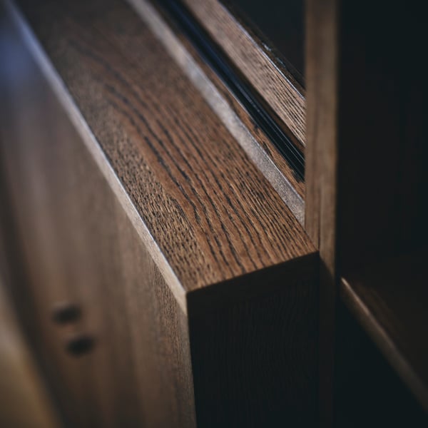 A close-up of the corner of a brown-stained oak veneer TONSTAD cabinet with doors shows details of the veneer and the edges.