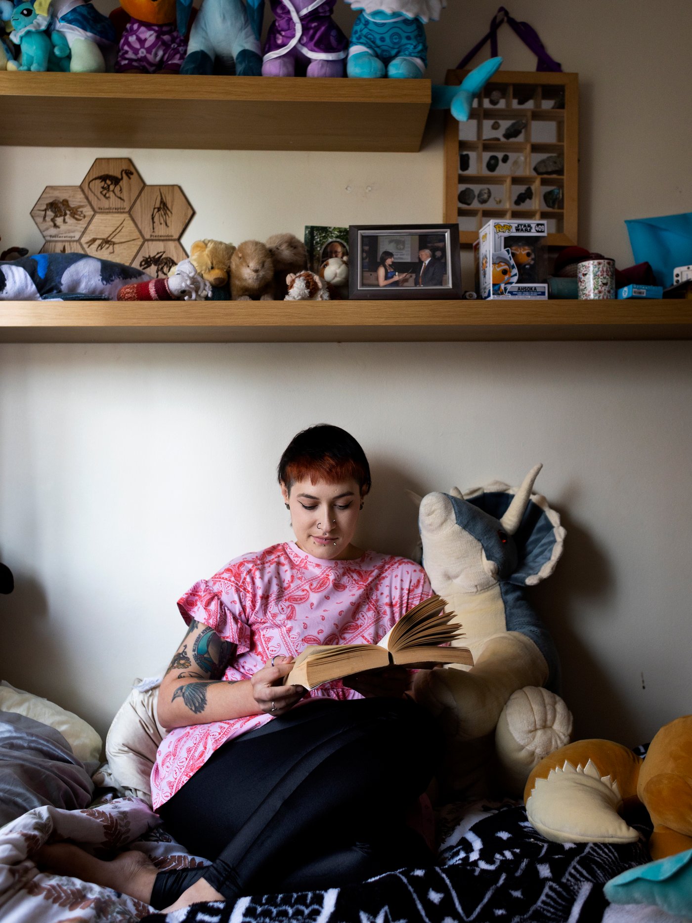 Woman sitting on her bed, surrounded by soft toys, reading a big book.