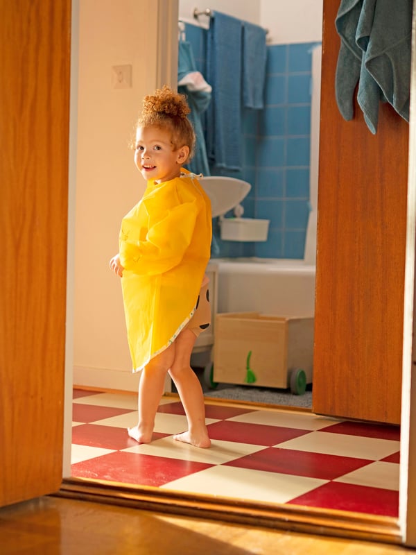 A small child in a yellow MÅLA apron standing in front of the bathroom.