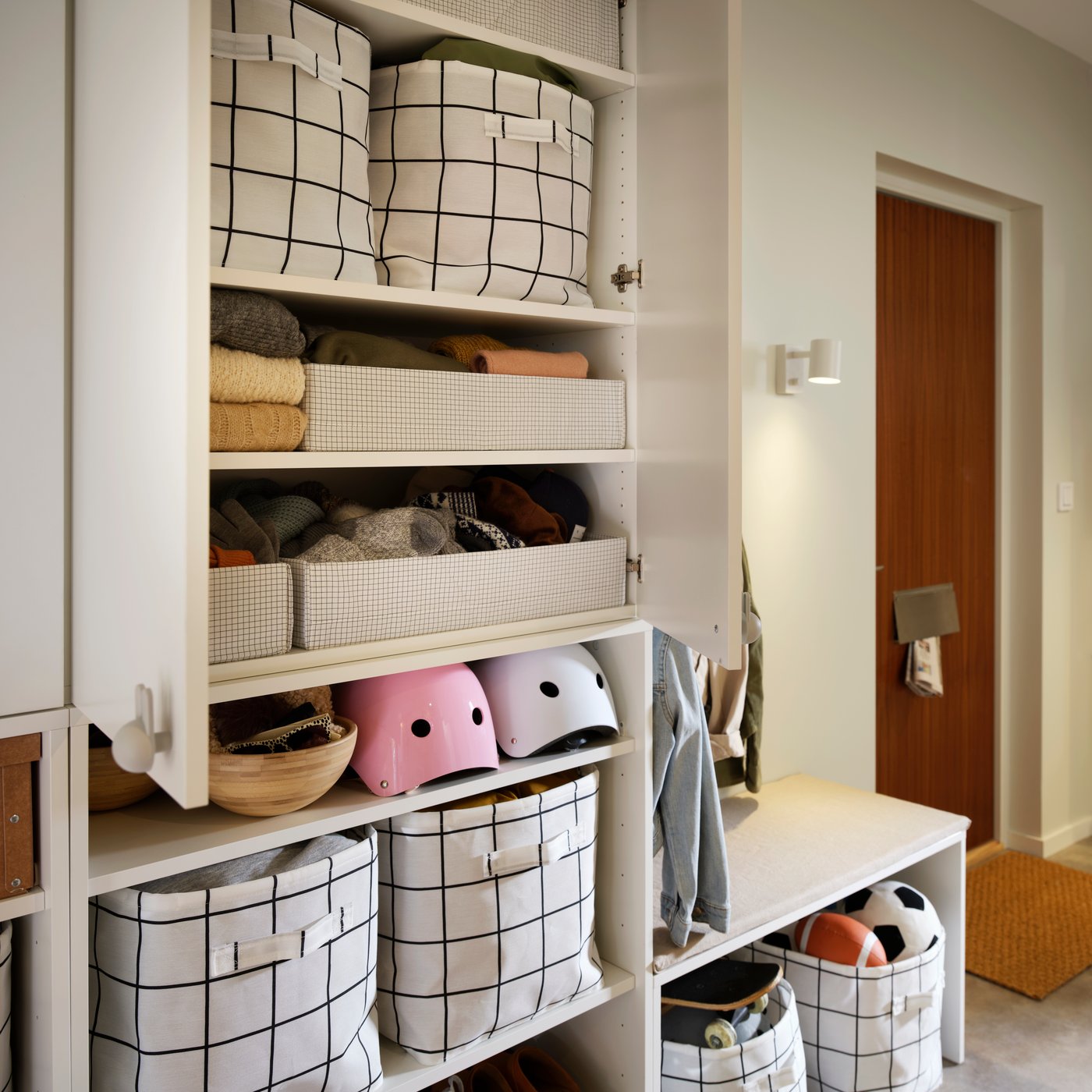 Une étagère de couloir sur laquelle sont disposés des paniers de rangement SLÄTTERVALL, à côté de casques et de linge plié.
