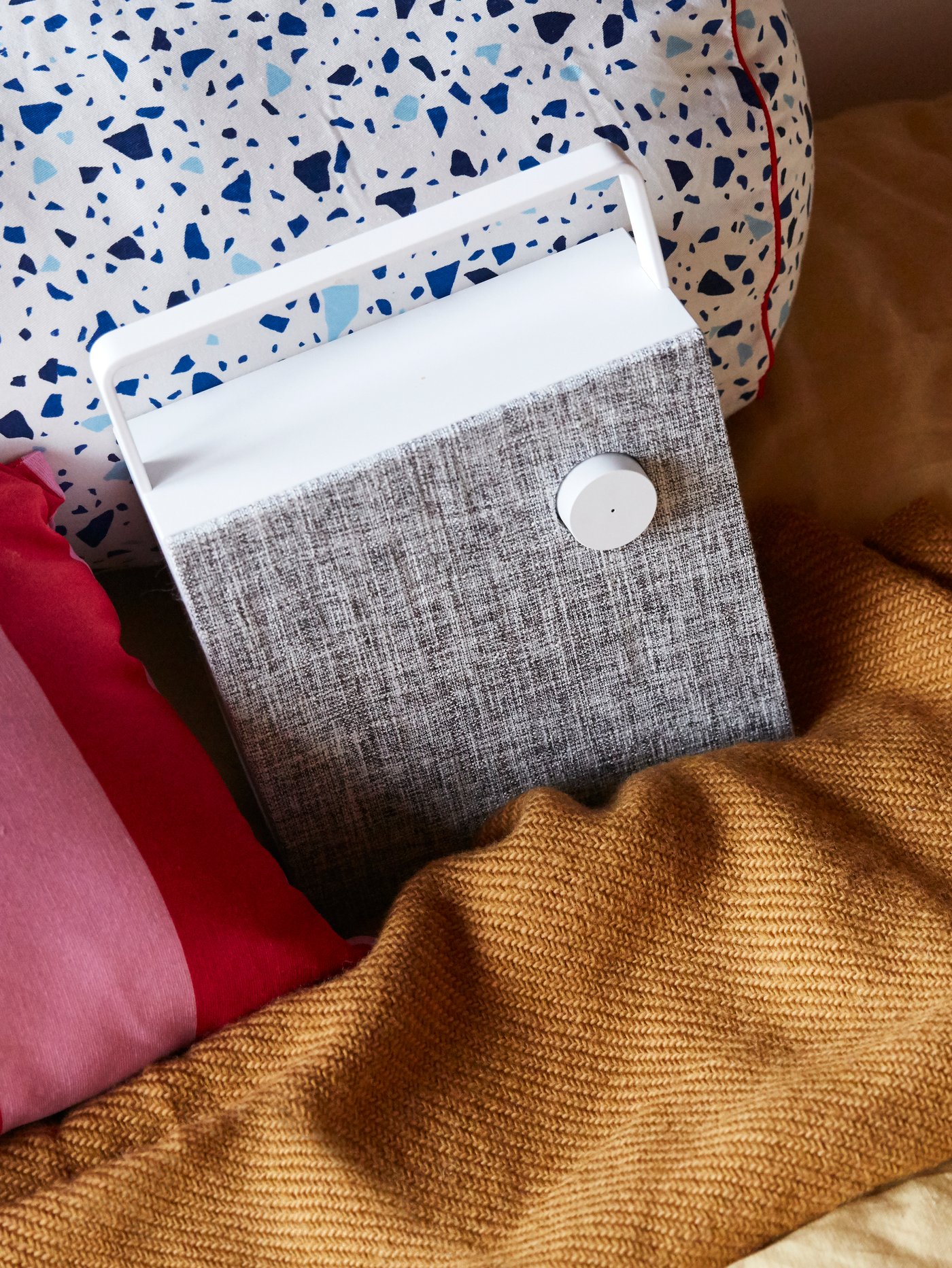 Hands placing a tablet on a white MÖJLIGHET headset/tablet stand, in front of an ENEBY Bluetooth speaker.