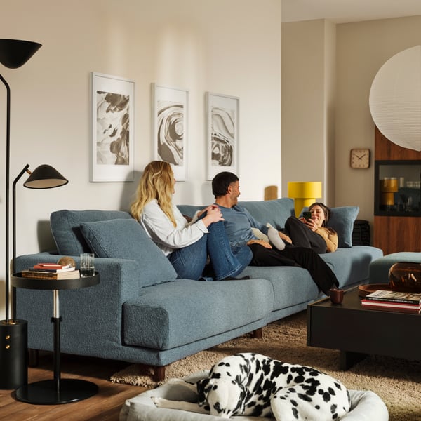 Three people lounge on a dark grey-blue UPPÅKRA 4.5-seat modular sofa near a TRANERED coffee table and a TRANERED side table.