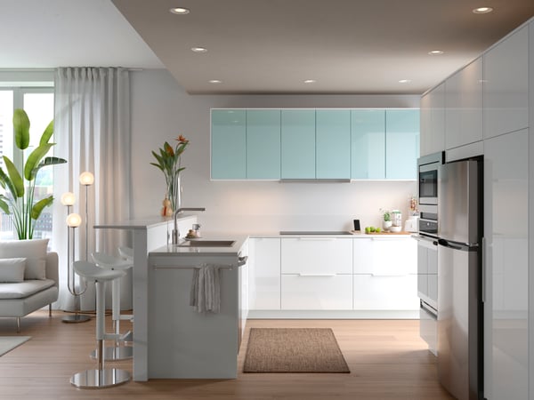 A SEKTION kitchen in white with a sink, a sofa, and on the wall are cabinets with JÄRSTA high gloss kitchen fronts in light turquoise.