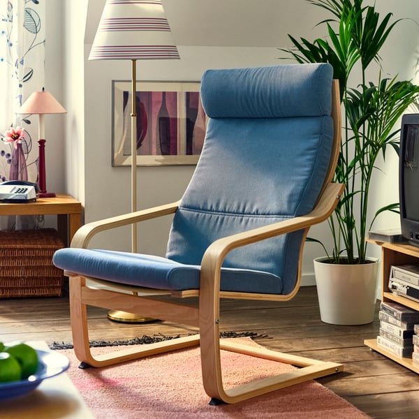 A 1990s-styled living room has a bentwood frame POÄNG armchair with a grey-blue cushion, on a fringed rug by a floor lamp.