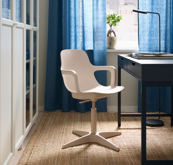 A beige ODGER swivel chair in the home office with blue curtains hanging for the window.