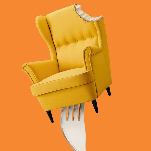 Fotoliu galben cu spătar înalt, ilustrat creativ ca un desert mușcat în partea de sus și înfipt într-o furculiță mare, pe fundal portocaliu – imagine jucăușă care sugerează combinația dintre confort și poftă de gustări.