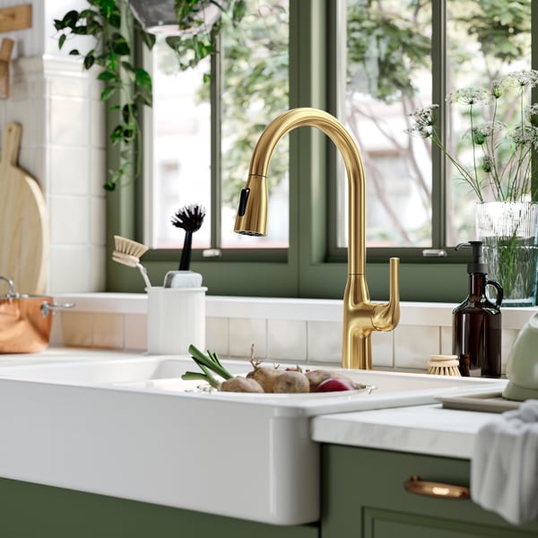 A MACKSJÖN kitchen faucets with a pull down-spray function in brass above a white sink in a green kitchen.