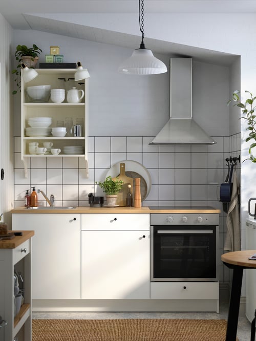 A kitchen with white tiles and grey walls, a white KNOXHULT kitchen with black knobs and appliances in stainless steel.