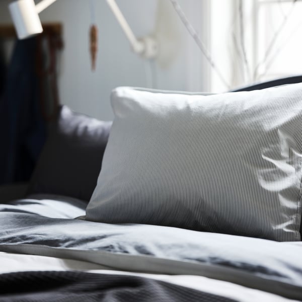 Un dormitorio con fundas nórdica y de almohada BLÅVINDA gris en la cama y una lámpara blanca en la pared de detrás.