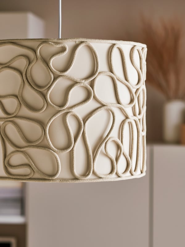 A pendant lamp with a beige VINGMAST lampshade with a curvy rope pattern that winds over a textile-covered inside.