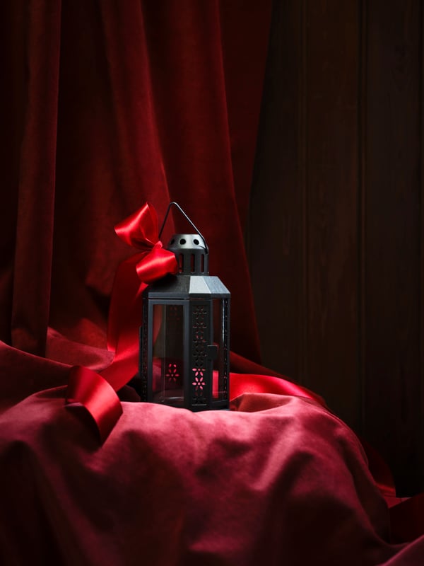 A black ENRUM lantern for tealight, in/outdoor in the living room on a red background.