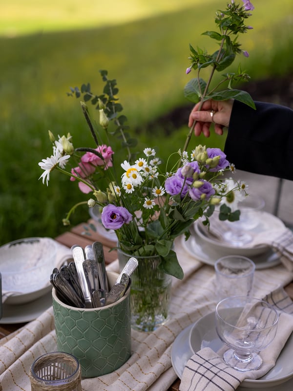 Et sommerbord i det fri dækket med blomster, tallerkener og bestik 