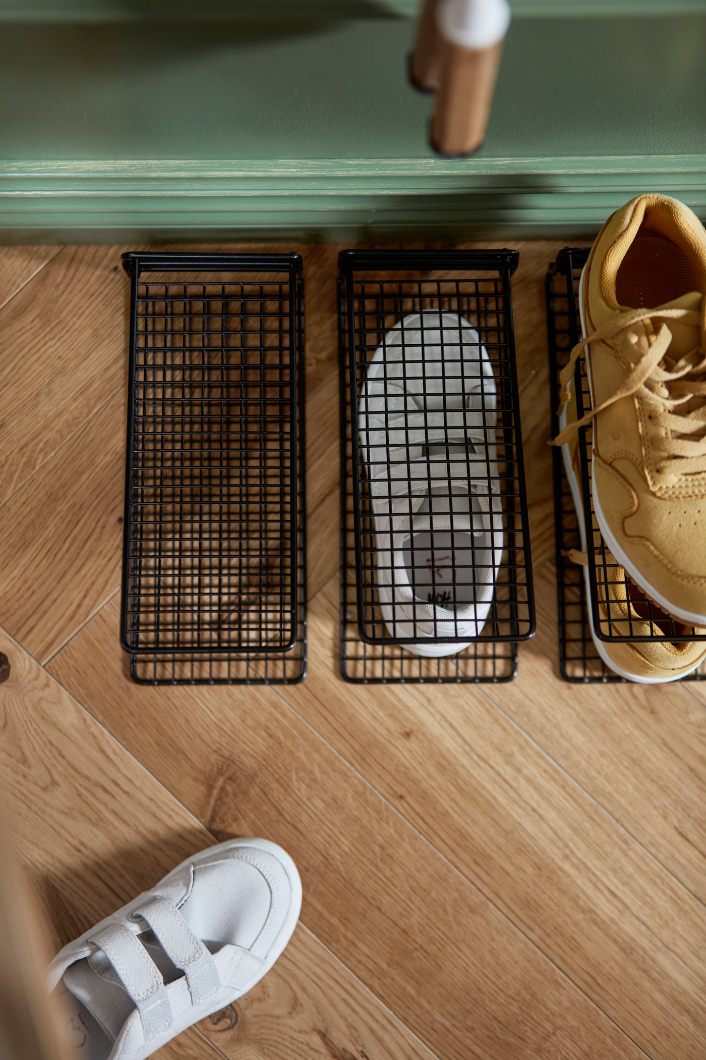 Tři černé úložné díly na boty SKOSTALL na podlaze v předsíni. Jeden z nich je obsazený teniskami.