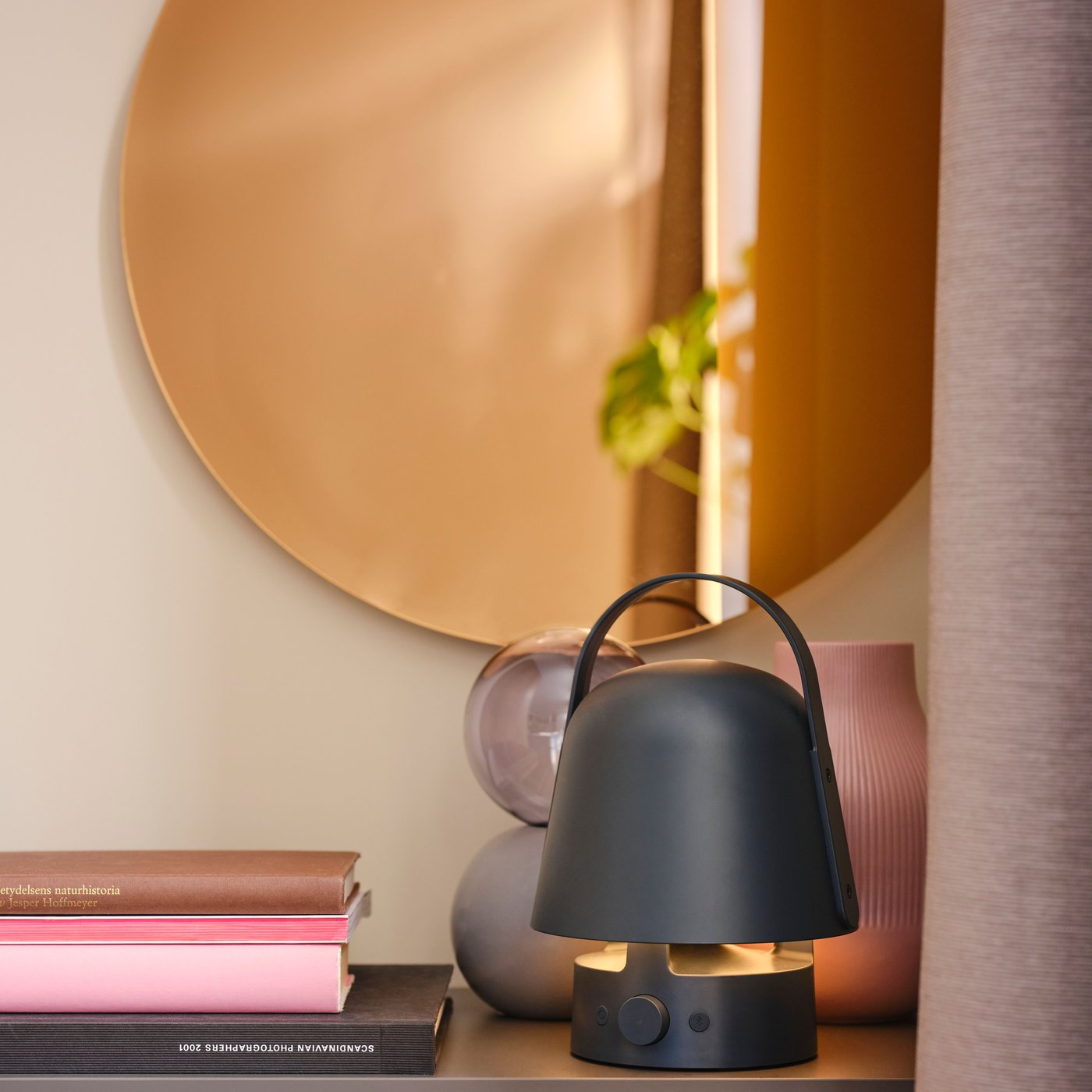 مصباح بمرآة/ جداري  VARMBLIXT LED دائري باللون البرونزي معلق فوق خزانة بها أغراض ديكور ومصباح بسماعة  في الأعلى.