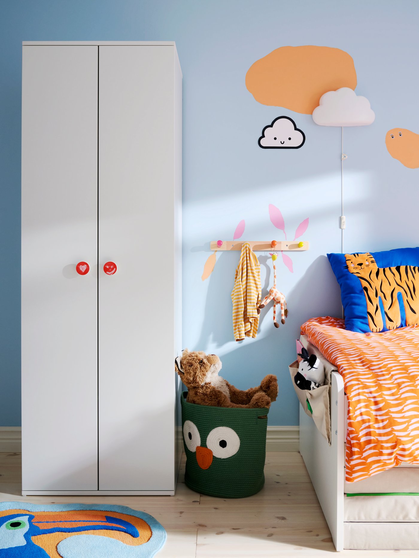 The foot-end of a SLÄKT bed by a light blue wall, with GODISHUS wardrobe to the left and wall-mounted hooks in between.