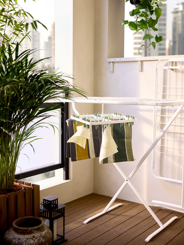 A white MULIG in/outdoor drying rack in a balcony corner has its two wings folded in with a hanging dryer on it.