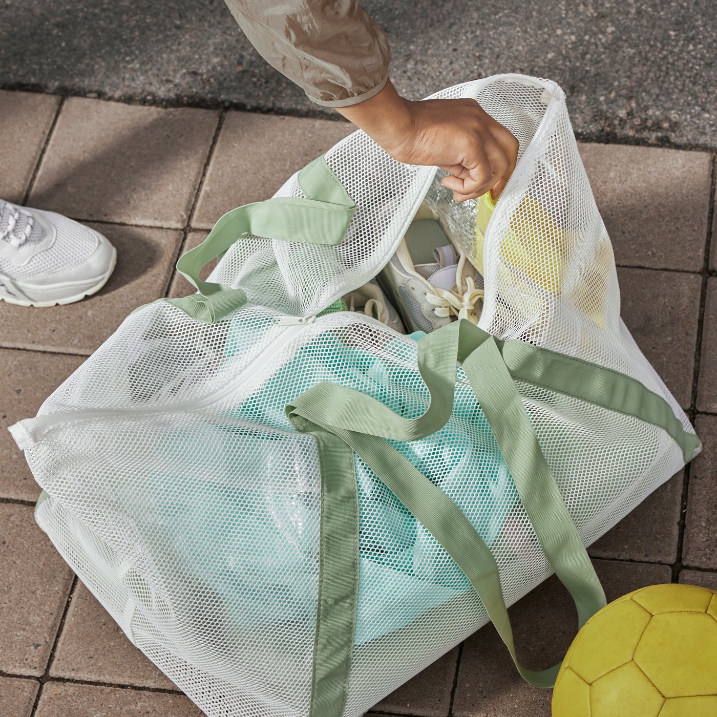 A DAJLIEN carrier bag sits on a tiled outdoor surface, full of items, with a hand reaching inside.