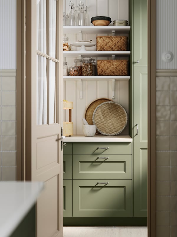 A door is open to a pantry with SEKTION base cabinets and white wall-mounted BERGSHULT shelves with jars and containers.