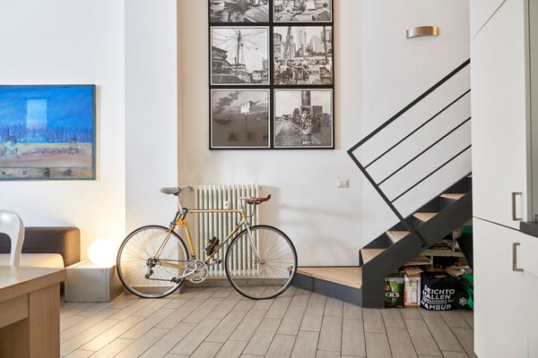 There is a bycicle in front of the stairs and frames on the wall