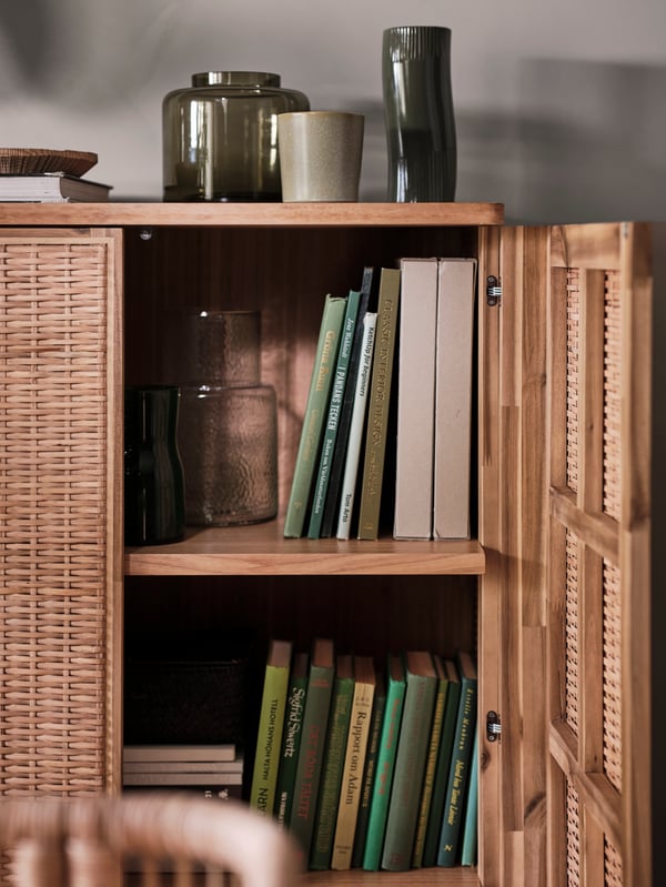 A FRYKSÅS cabinet has its right door open, revealing books and decorative glassware on the shelves inside.