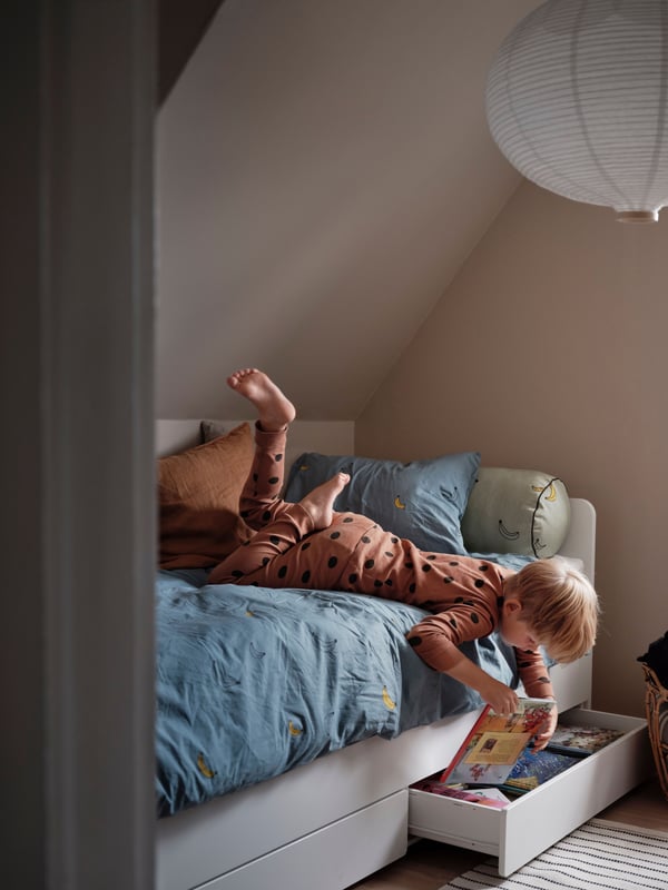 Enfant rangeant ses affaires dans un tiroir de rangement sous le lit SLÄKT