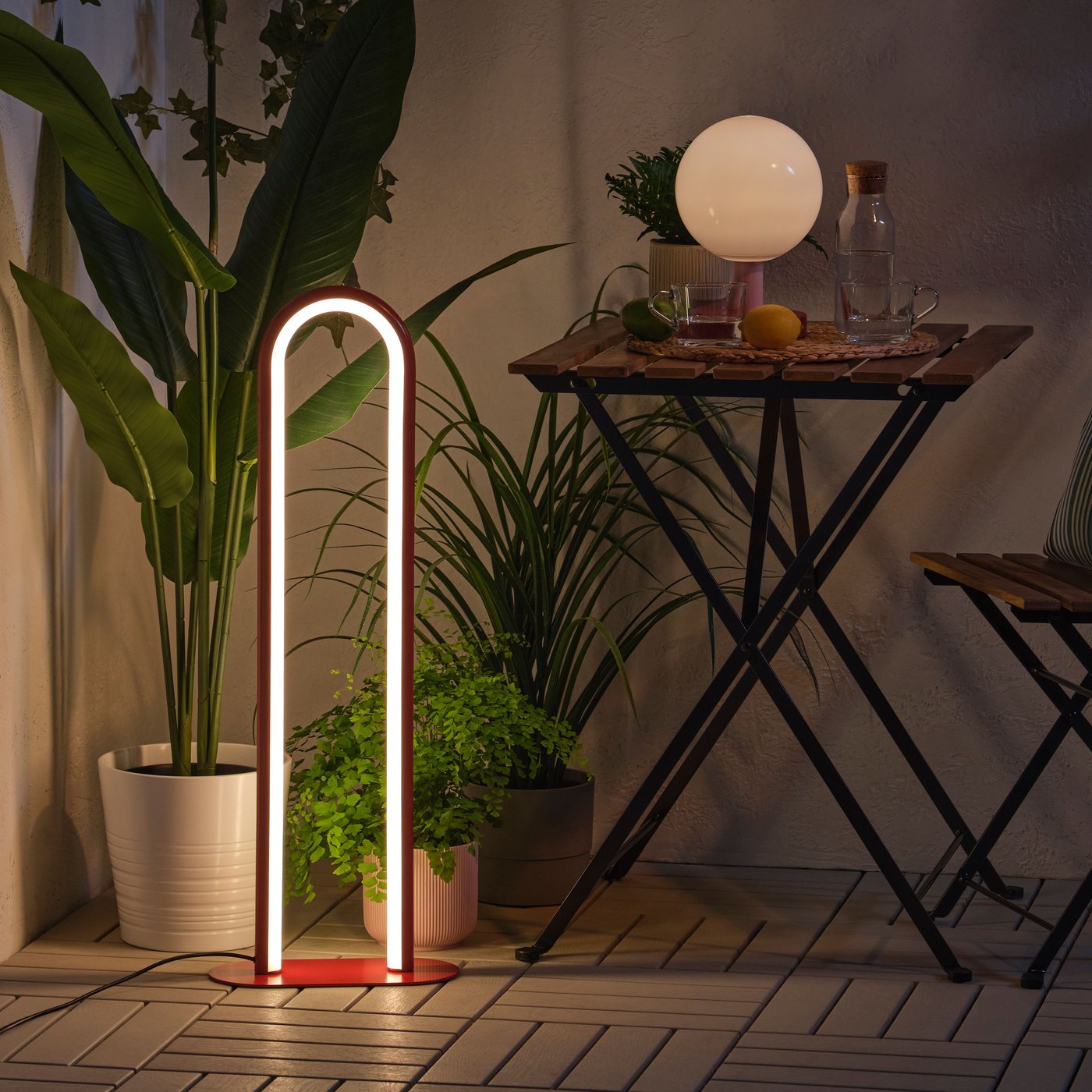 A dimmable red SOLVINDEN floor lamp creates a snug mood in the dark, surrounded by green plants and a balcony table.