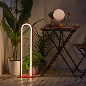 A dimmable red SOLVINDEN floor lamp creates a snug mood in the dark, surrounded by green plants and a balcony table.