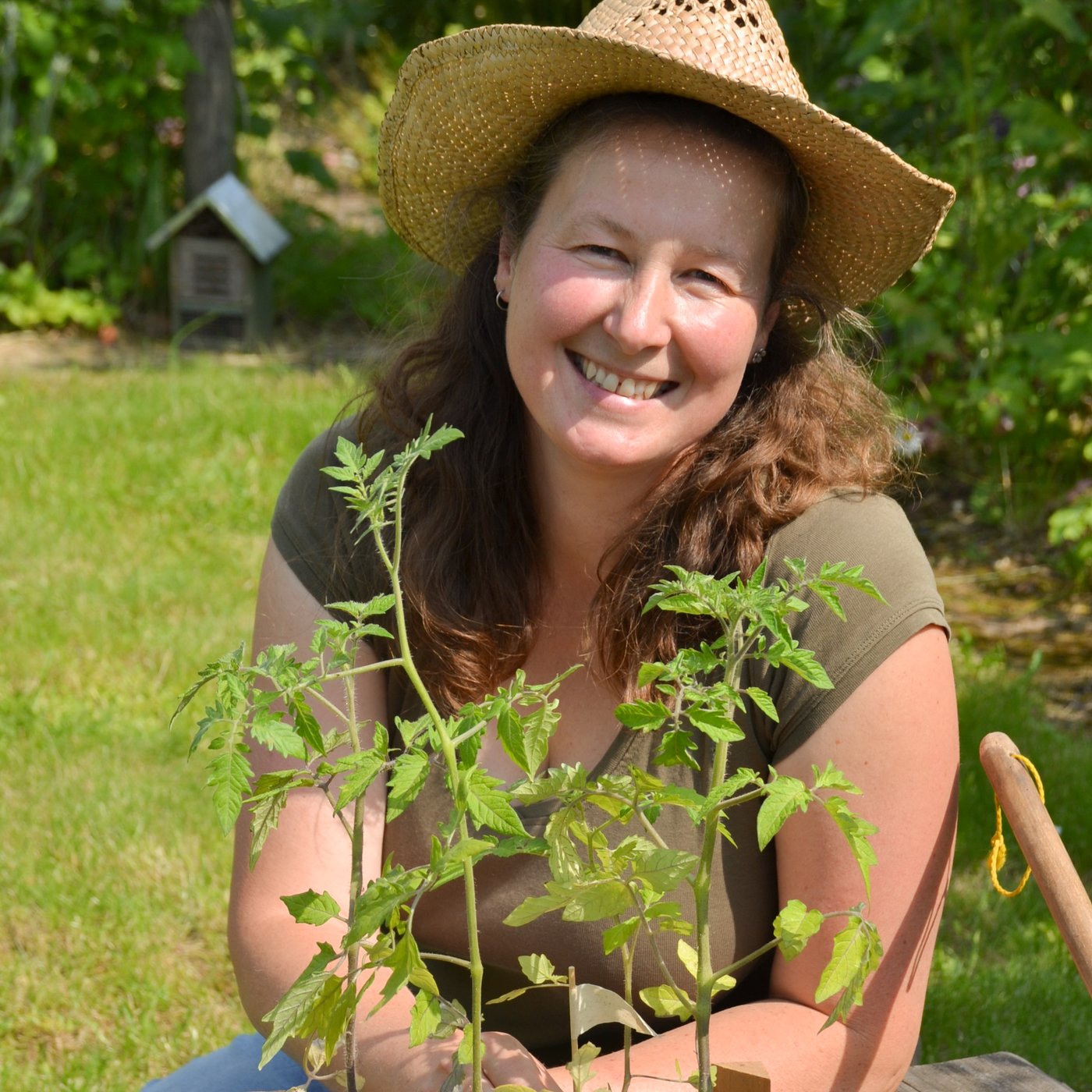 Eine Frau sitzt im Garten vor einer Pflanze und lacht