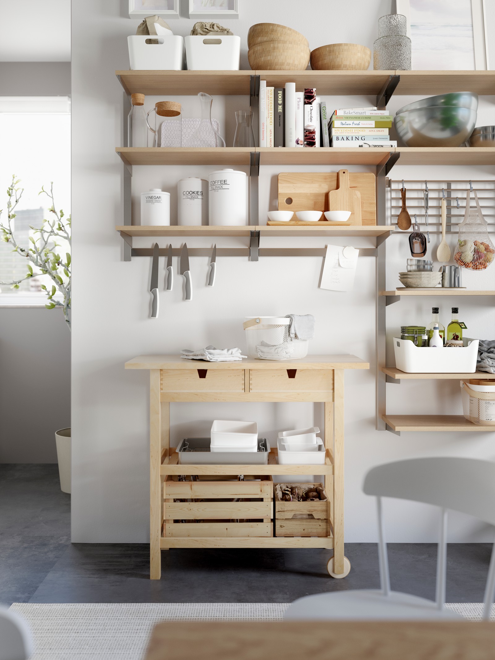 Drvena kuhinjska kolica u skandinavskom deko stilu s fiokama i drvenim kutijama, s otvorenim policama iznad, na kojima se nalaze rustični kuhinjski pribor, metalne činije za kuvanje, keramičke tegle za odlaganje i stakleni bokali za vodu.
