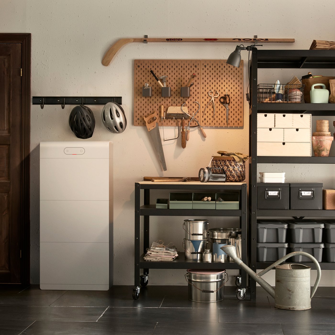 Un espace de travail bien organisé avec un tableau perforé rempli d'outils, des étagères de rangement avec des pots et des boîtes de conserve, une armoire blanche et une étagère avec deux casques.