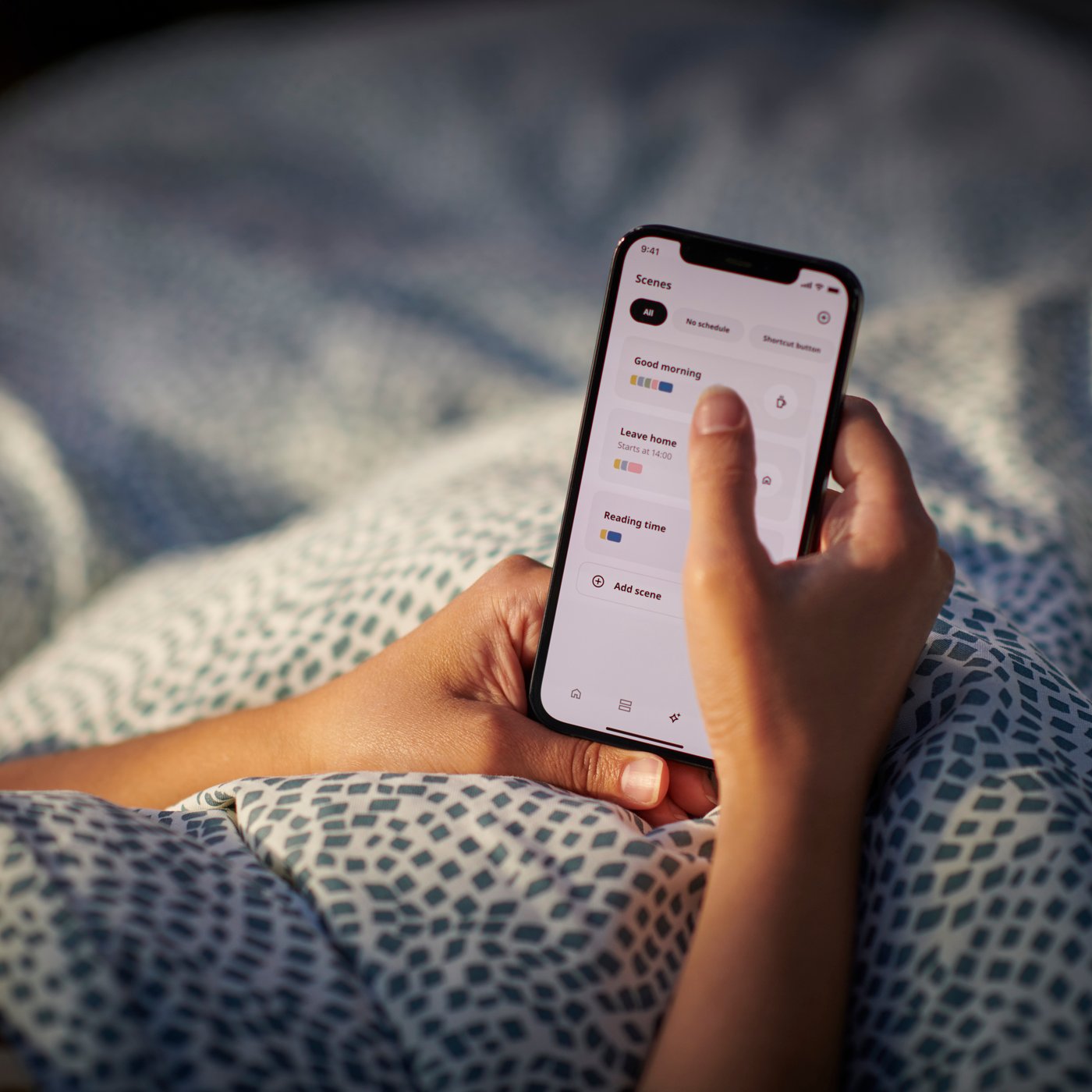 A person's hands holding a mobile device while laying tucked in under a dotted duvet.