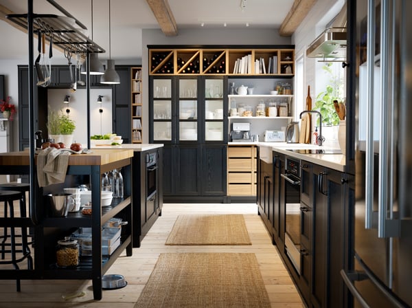 Een zwarte keuken met een houten vloer, wit keukeneiland, zwarte kasten en wijn in een open wijnrek.