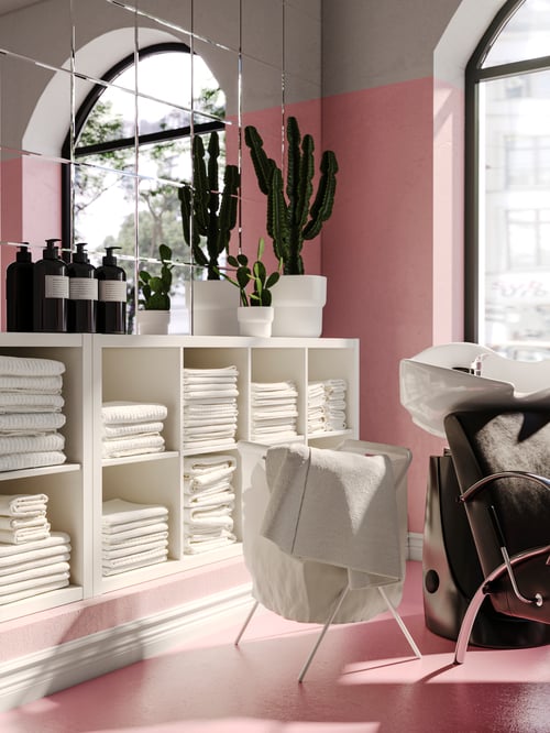 Two white KALLAX shelving units placed horizontally against a mirror wall, filled with white towels and with bottles on top.