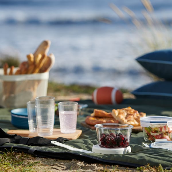 Manta de color verde con articulos de picnic encima, como potes de vidrio, vasos de plástico y comida.