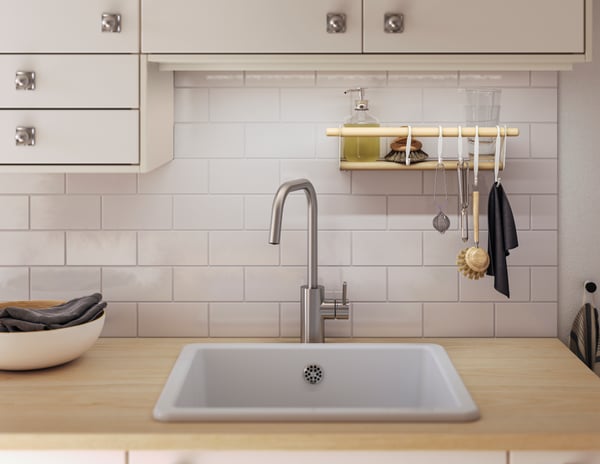 A kitchen with white tiles, white wall cabinets, a white sink and a wooden worktop. 