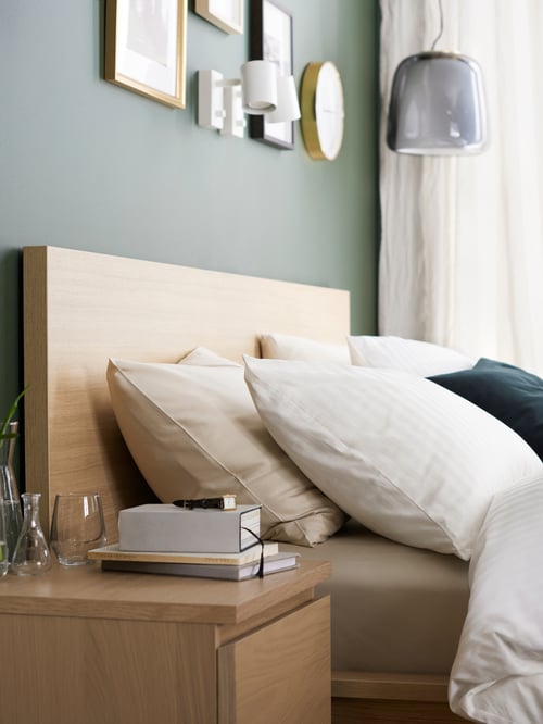 The side view of bedside table and a white stained oak veneer MALM bedframe with soft bedding in a dark green bedroom.
