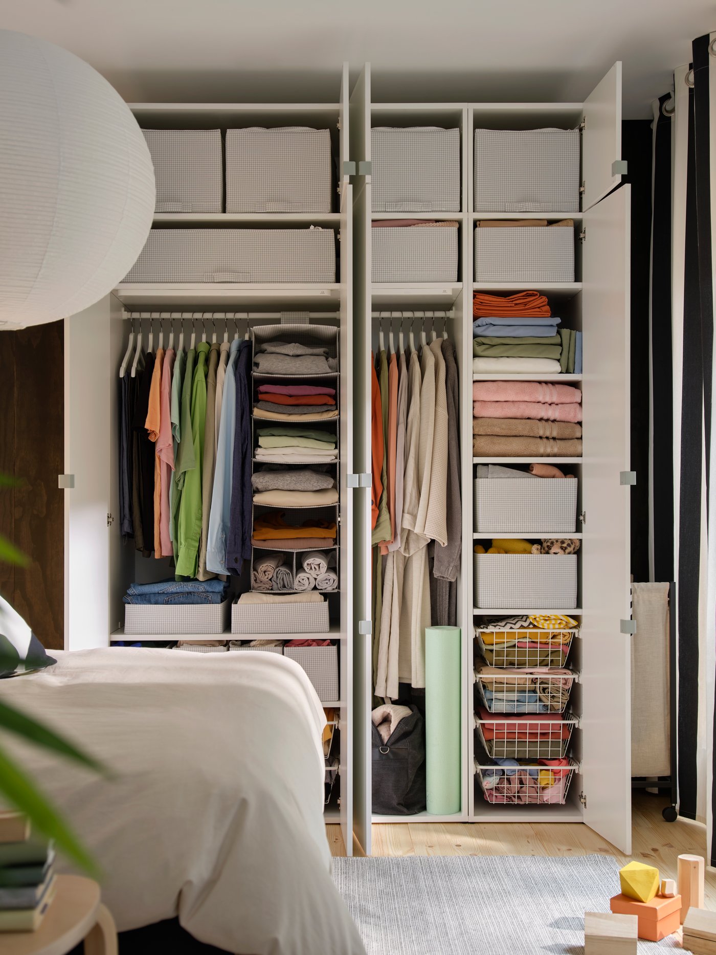 Contenitori STUK bianchi disposti sugli scaffali e all'interno di cestini in filo metallico in una composizione di armadi LASTARE in una camera da letto.