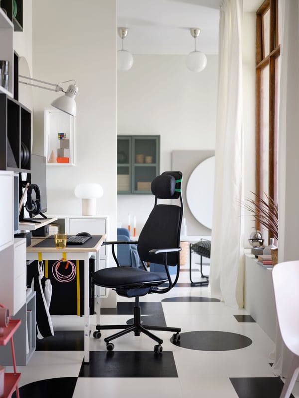 A dark grey LÖPARBANA gaming chair is rolled out from a PC gaming setup in a passageway with modern, geometric decor.