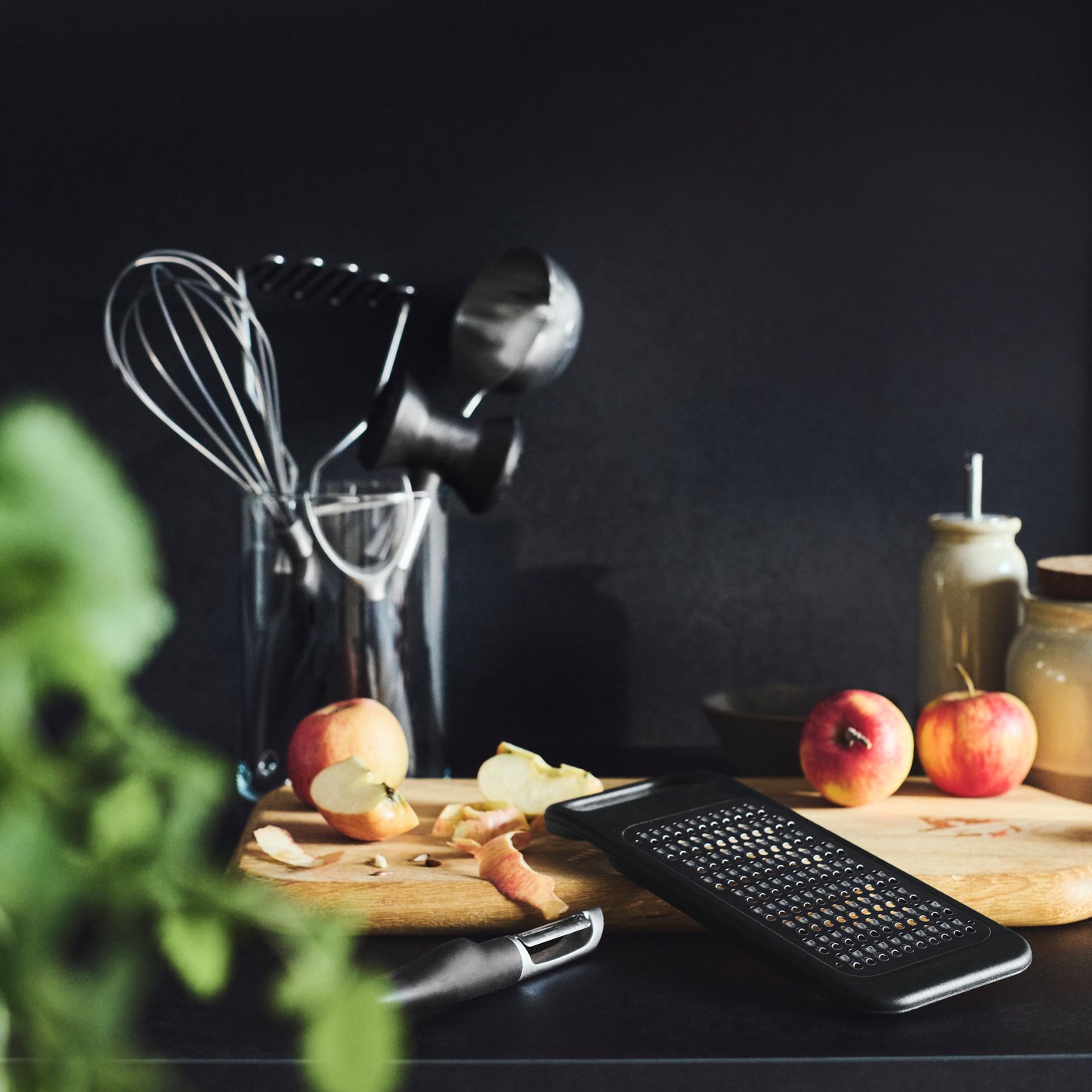 An IKEA 365+ grater and potato peeler next to a partially peeled and sliced apple and a vase full of IKEA 365+ utensils.