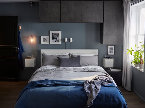 MALM queen sized bed frame with BESTA cabinets on wall above the bedframe, next to a window with light filtering curtains. 