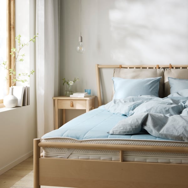 Close-up of foot end of a bed in brushed oak with a matching bedside table. Cooling mattress protector on the bed.