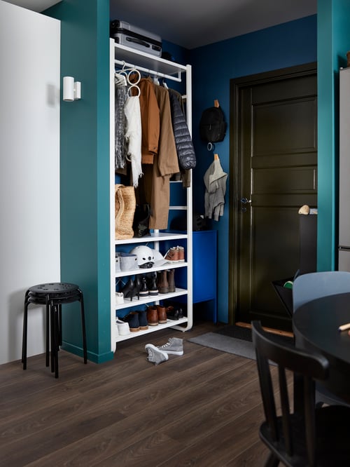 Entrance with white steel storage system containing shoes, coats and accessories, and a stack of black stools next to it.