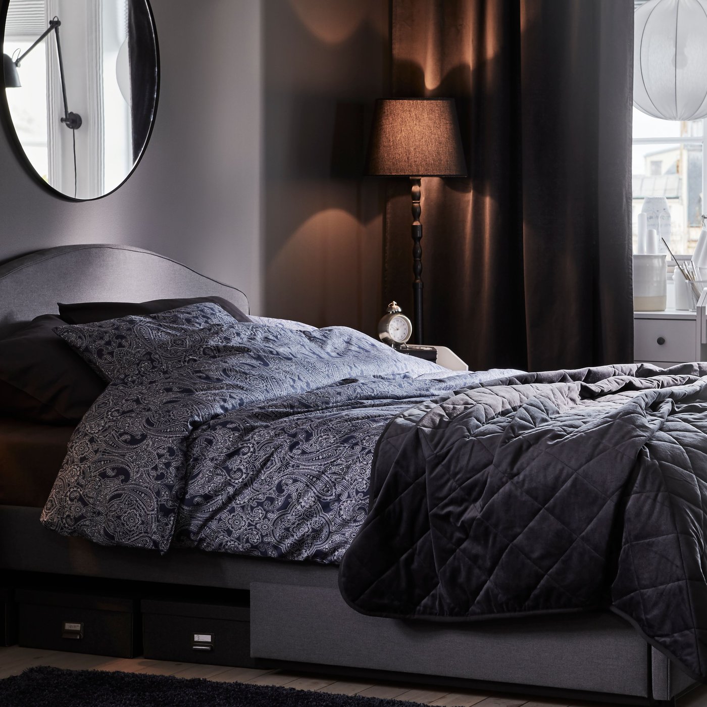 Un letto imbottito HAUGA grigio con biancheria da letto JÄTTEVALLMO e copriletto MJUKPLISTER contro la parete di una camera.