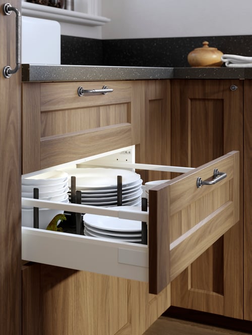 An open kitchen drawer with a brown walnut-effect ENKÖPING front and SKRUVSHULT handle with piles of plates and bowls inside.