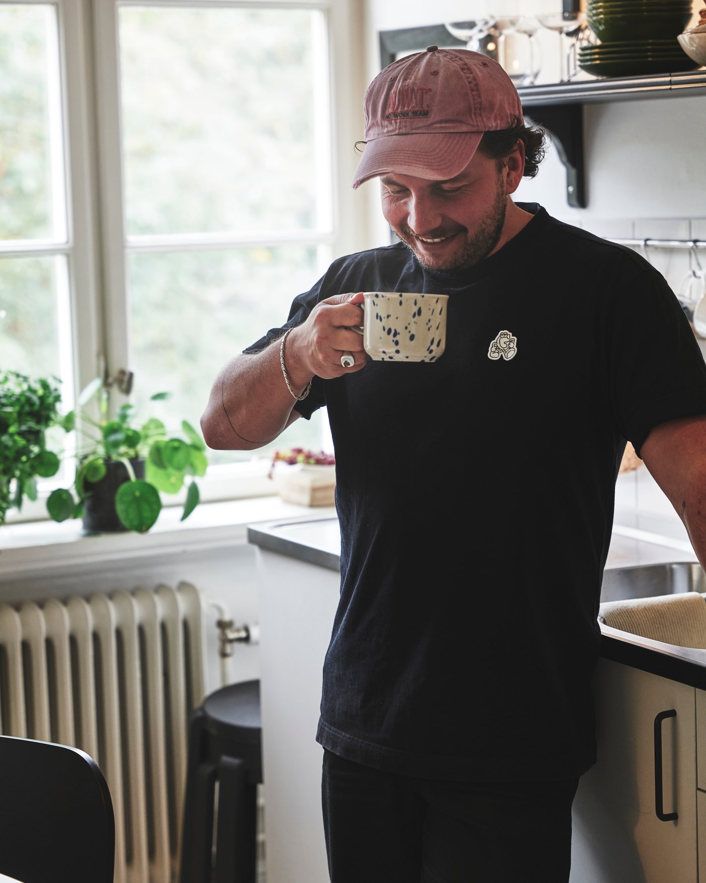 En person står lutad mot en bänkskiva i ett kök med en mugg i handen.