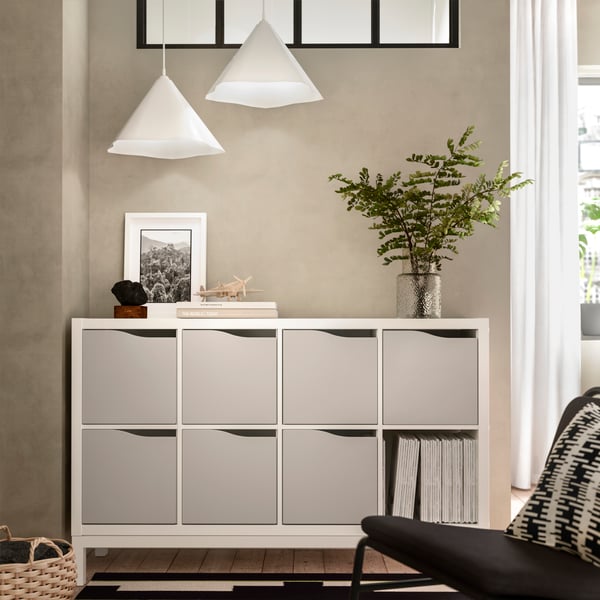 A section of a light room with a wall-mounted KALLAX shelving unit fitted with inserts with doors and decorations on top.