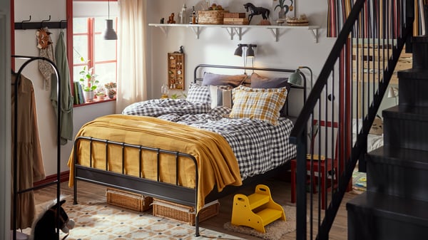 Chambre à coucher familiale avec structure de lit STJÄRNÖ en anthracite avec draps à carreaux. Couverture et détails en jaune vif.