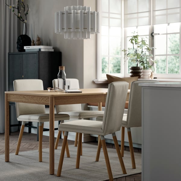 A TONSTAD extendable table in oak veneer set in a dining space with four grey chairs and natural light from large windows.