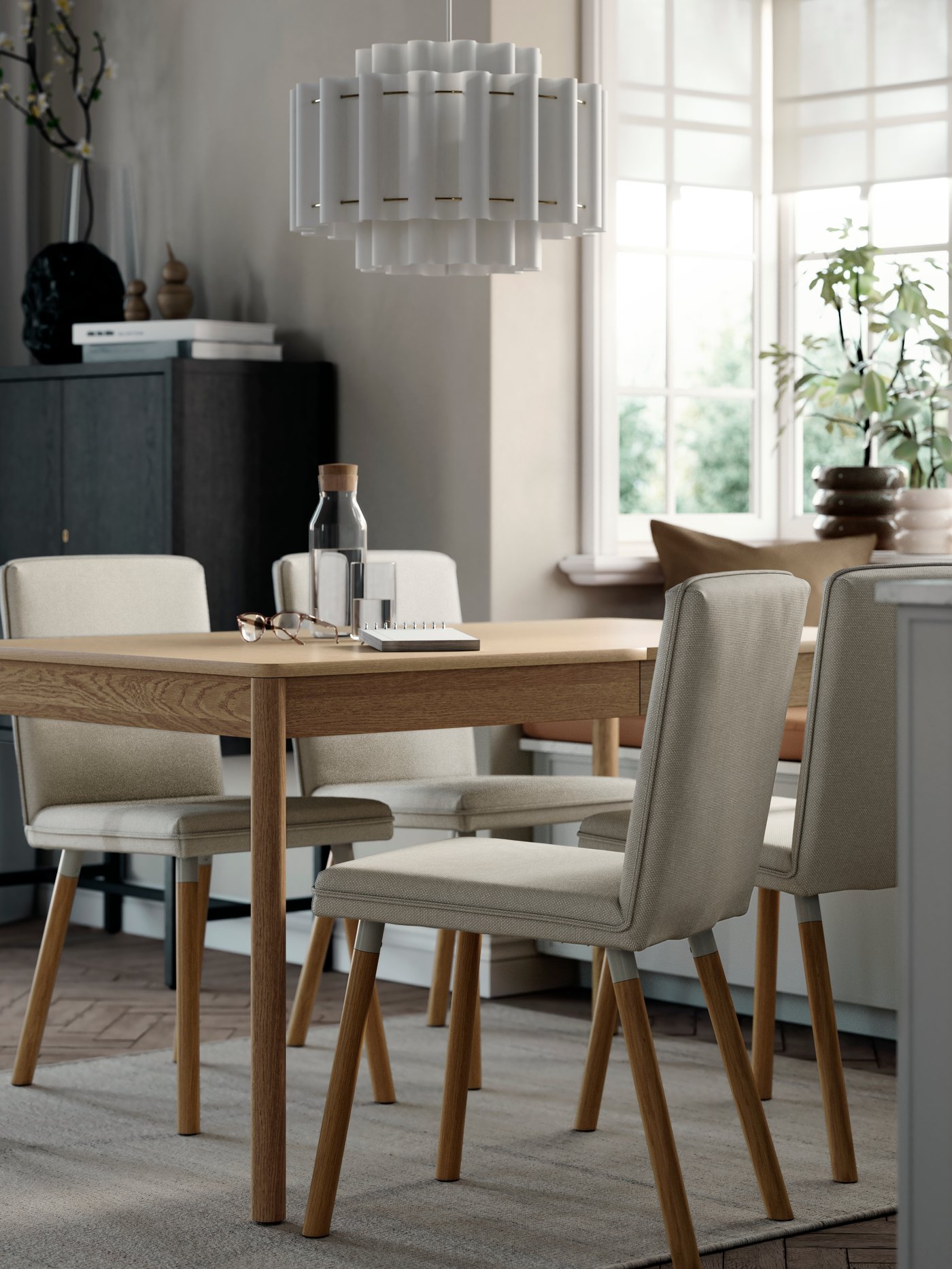 A TONSTAD extendable table in oak veneer set in a dining space with four grey chairs and natural light from large windows.