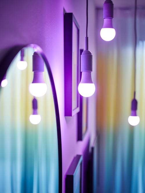 Multiple lit purple TRÅDFRI LED bulbs, hanging from the ceiling with cord sets and placed near a mirror.